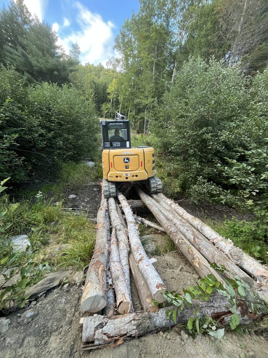 Homestead Heroes John Deere excavator on log road in Maine forest